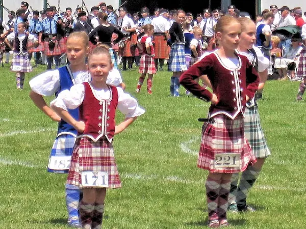 Children dancing in traditional dress at the Highland Games, wearing numbers for competition.