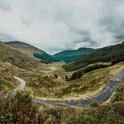 Scenic winding road through the picturesque village of Drumnadrochit, surrounded by lush greenery.