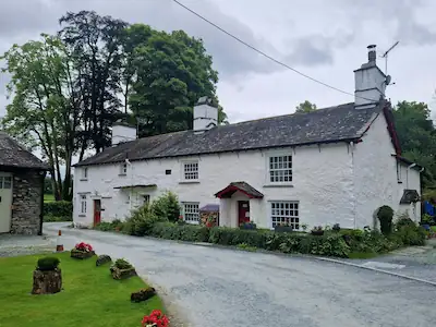 A spacious white stone cottage known as the Old Mill House, surrounded by lush gardens in a picturesque setting.