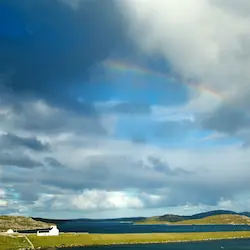 Vibrant landscape of the Isle of Lewis, showcasing rolling land, sparkling water, and a vivid rainbow.
