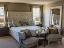 A modern and comfy bedroom featuring a kingsize bed, two chairs, a table, a large mirror, and abundant natural light.