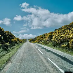 A long, straight road connecting the northernmost towns of John O'Groats and Thurso, surrounded by open fields and expansive skies.
