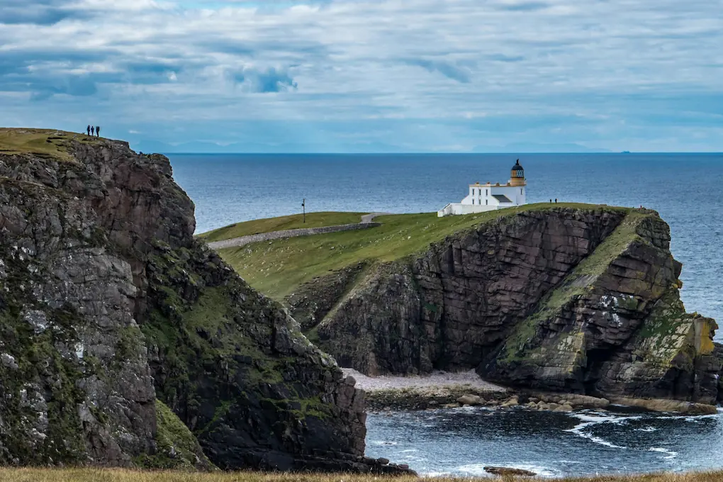 Stoer Lighthouse standing prominently on a rugged cliffside, overlooking the vast coastal landscape.