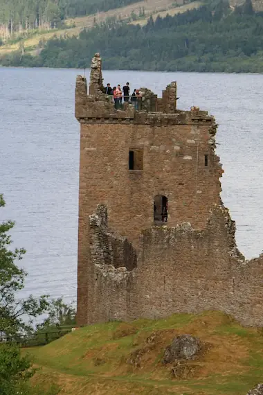 The majestic ruins of Urquhart Castle overlooking Loch Ness, surrounded by lush greenery and dramatic landscapes.