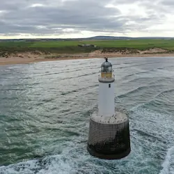 The scenic coastline of Rattray, featuring sandy shores and rolling waves beneath a cloudy sky.